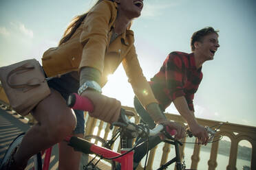 Happy couple riding bicycle against sky during sunny day - AJOF00517