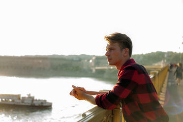 Contemplating man looking away while standing by railing on bridge against clear sky - AJOF00518