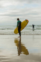 Jugendlicher mit Surfbrett und männlichem Freund, der am Strand im Meer steht - AJOF00522