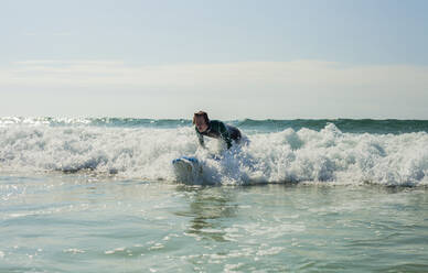 Teenage boy surfing in sea against sky at beach  - AJOF00524