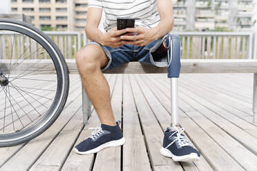 Low section of man with artificial limb using mobile phone in city - JCZF00329