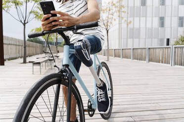 Low section of man with artificial limb using mobile phone on bicycle in city - JCZF00332