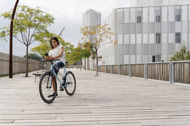 Lächelnder Mann mit Beinprothese benutzt Handy auf dem Fahrrad in der Stadt - JCZF00333