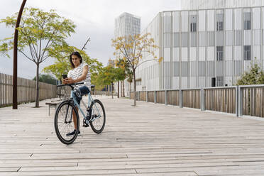 Smiling man with artificial limb using mobile phone on bicycle in city - JCZF00333