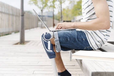 Midsection of man with artificial limb using laptop in city - JCZF00335