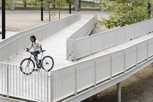 Hohe Winkel Ansicht der lächelnden amputierten Mann mit Handy auf dem Fahrrad über Brücke in der Stadt - JCZF00338