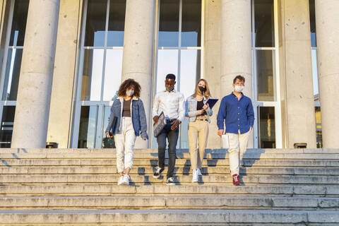 University students wearing protective face mask while moving down on staircase against education building stock photo