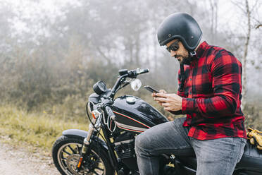 Mann benutzt sein Smartphone auf dem Motorrad sitzend während einer Autofahrt - DGOF01577