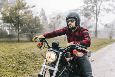 Männlicher Biker mit Motorrad auf unbefestigtem Weg bei nebligem Wetter am Wochenende - DGOF01583