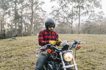 Männlicher Motorradfahrer trägt Handschuhe, während er im Wald auf dem Motorrad sitzt - DGOF01587