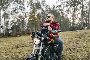 Männlicher Motorradfahrer mit Sonnenbrille auf einem Motorrad im Wald sitzend - DGOF01588