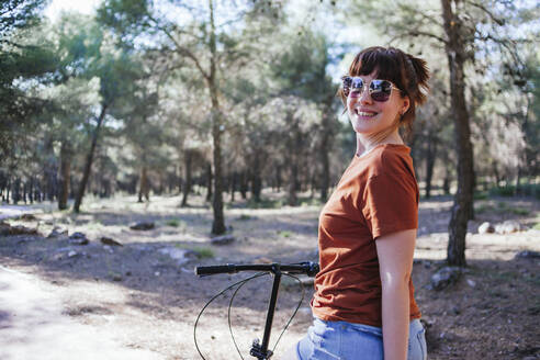 Smiling young woman in sunglasses with bicycle at countryside during weekend - MGRF00034