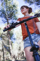 Junge Frau schaut weg, während sie mit dem Fahrrad in der Landschaft steht - MGRF00043