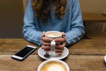 Frau mit Kaffeetasse am Tisch sitzend - JMPF00511