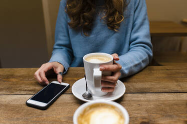 Frau mit Smartphone trinkt Kaffee am Tisch - JMPF00512