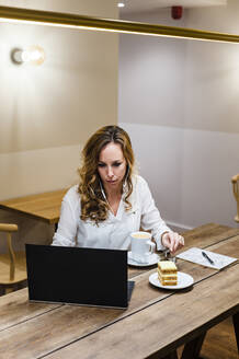 Geschäftsfrau, die einen Laptop benutzt, während sie am Tisch Kaffee trinkt - JMPF00517