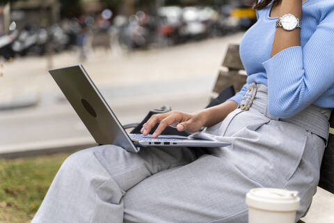 Frau surft im Internet auf einem Laptop, während sie auf einer Bank sitzt, lizenzfreies Stockfoto