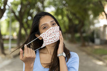 Beautiful woman wearing protective face mask in park during COVID-19 - AFVF07527