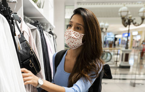 Woman wearing protective face mask while looking at clothes in shopping mall stock photo