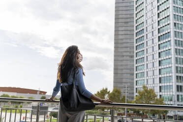 Rückansicht einer Frau mit Handtasche, die während der COVID-19-Pandemie in der Stadt an einem Geländer steht - AFVF07551