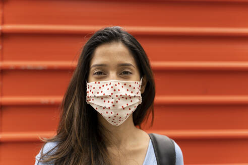 Contemplating woman with protective face mask standing against shutter during COVID-19 - AFVF07565