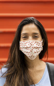 Smiling woman with protective face mask standing against shutter during COVID-19 - AFVF07566