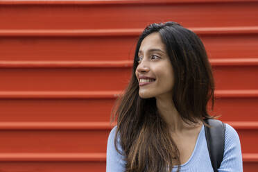 Lächelnde, selbstbewusste Frau, die vor einem orangefarbenen Fensterladen wegschaut - AFVF07568