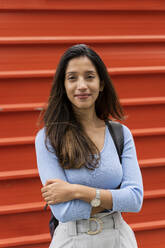 Smiling confident woman with arms crossed standing against shutter - AFVF07569