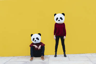 Männliche und weibliche Freunde in Pandamaske vor gelber Wand - XLGF00770