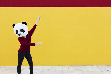 Frau mit Pandamaske tanzt gegen eine gelbe Wand - XLGF00774
