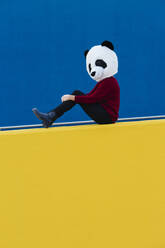 Frau mit Panda-Maske, die an einer blauen Wand sitzt - XLGF00776