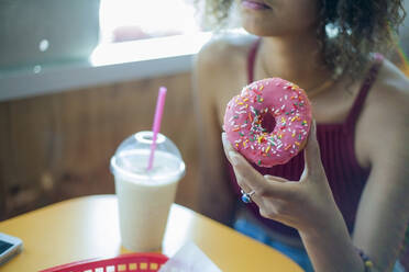 Junge Frau isst Donut in einem Café - AJOF00529