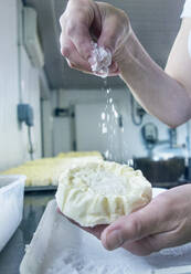 Frauenhand, die in einer Molkerei Mehl auf Käse streut - AJOF00533