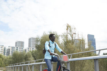 Mature man looking away while commuting on bicycle against sky in city - PMF01516