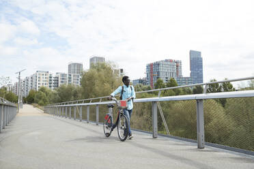 Man walking with bicycle on road against sky in city - PMF01517