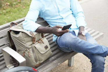 Mann hält Smartphone, während er auf einer Bank sitzt - PMF01522