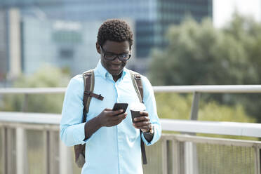 Lächelnder Mann mit Textnachrichten auf einem Smartphone in der Stadt stehend - PMF01527