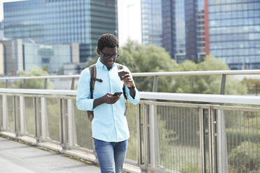 Mann mit Smartphone und Einweg-Kaffeebecher auf dem Gehweg in der Stadt - PMF01528