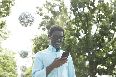 Älterer Mann, der eine SMS auf seinem Smartphone schreibt, während er über Kopfhörer Musik hört, steht im Park - PMF01532