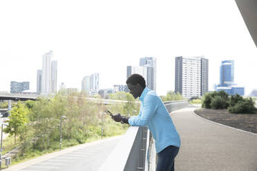 Mature man using smart phone standing on footpath in city - PMF01534