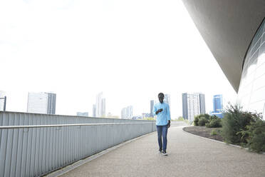 Lächelnder Mann, der ein Smartphone benutzt, während er auf einem Fußweg in der Stadt spazieren geht - PMF01538