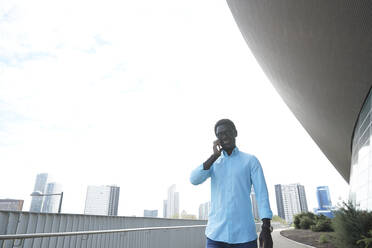 Mann schaut weg, während er mit seinem Smartphone gegen den klaren Himmel in der Stadt spricht - PMF01540
