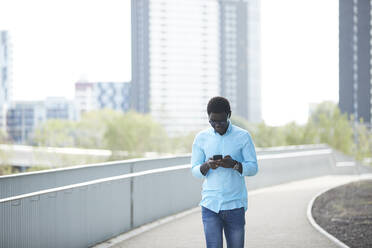 Mature man using smart phone standing on footpath in city - PMF01542