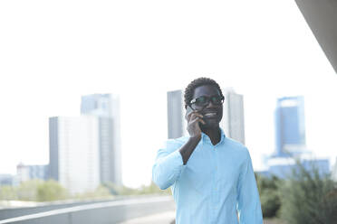 Smiling man talking on smart phone standing against clear sky - PMF01543