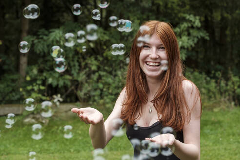 Glückliche Frau spielt mit Seifenblasen im Hinterhof - LBF03260