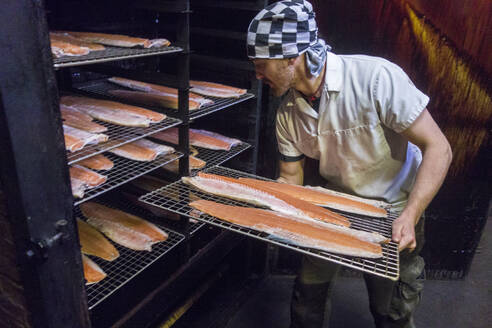Arbeiter, der eine Fischschale in die Räucherkammer einer Lebensmittelfabrik einlegt - AJOF00543