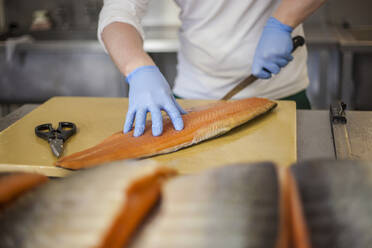 Mann schneidet Fisch an der Theke in einem Lebensmittelverarbeitungsbetrieb - AJOF00545
