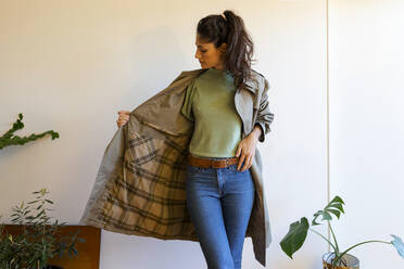 Female model wearing jacket standing against wall at home - VABF03832