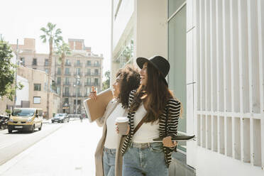 Businesswomen laughing while looking away standing on street in city during sunny day - VABF03900