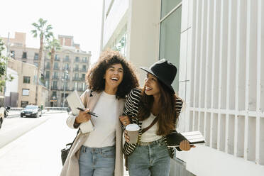 Businesswomen laughing while walking on street during sunny day - VABF03901